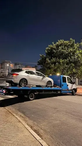 Guincho plataforma transportando carro sedã à noite